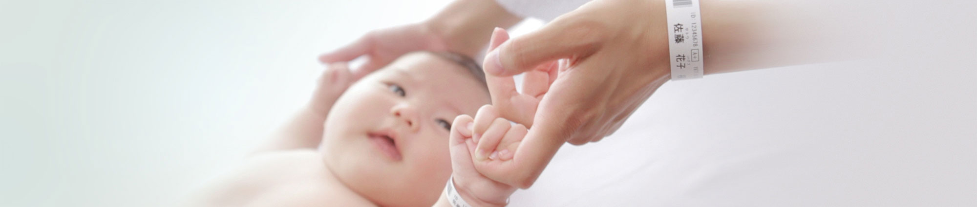 Baby in einem Krankenhaus, das den Finger seiner Mutter hält – beide tragen ein Patientenarmband