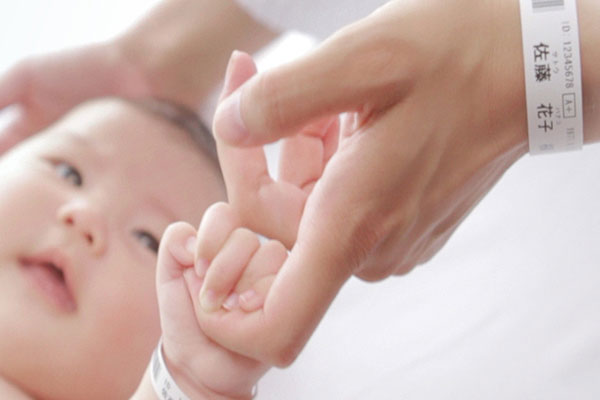 Baby in einem Krankenhaus, das den Finger seiner Mutter hält – beide tragen ein Patientenarmband